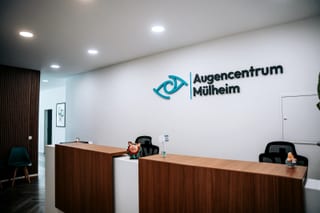 Empfang der Praxis Styrum mit Holztheke, Holzlamellenwand und Augencentrum-Mülheim-Logo an der Wand
